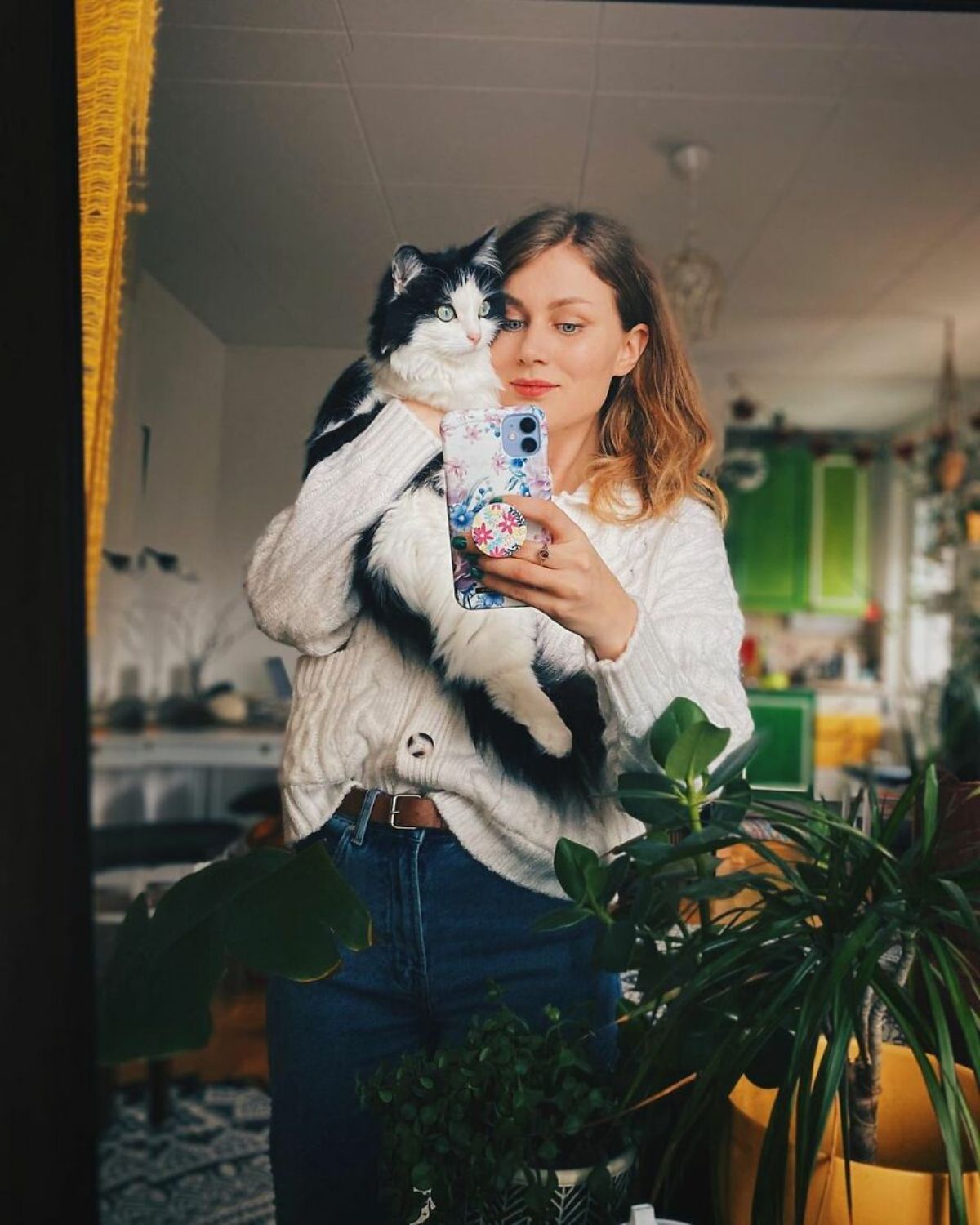 a woman taking a mirror selfie holding a black and white fluffy cat