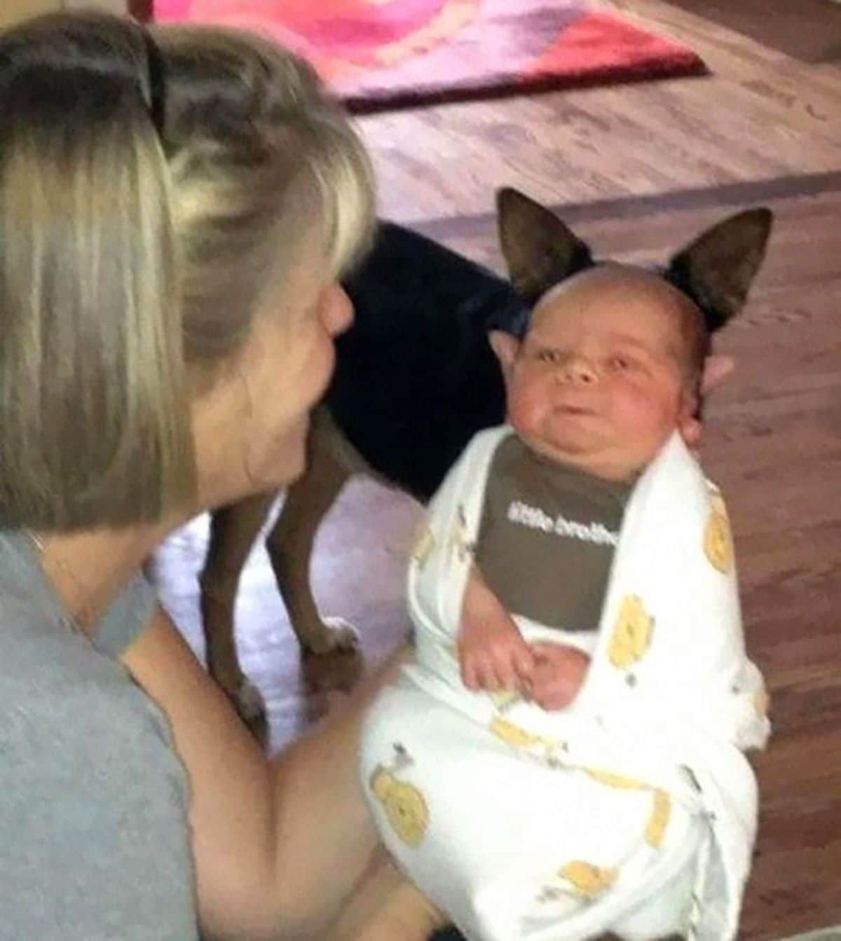 woman holding a baby with a black and brown dog right behind the baby looking like the baby has dog ears