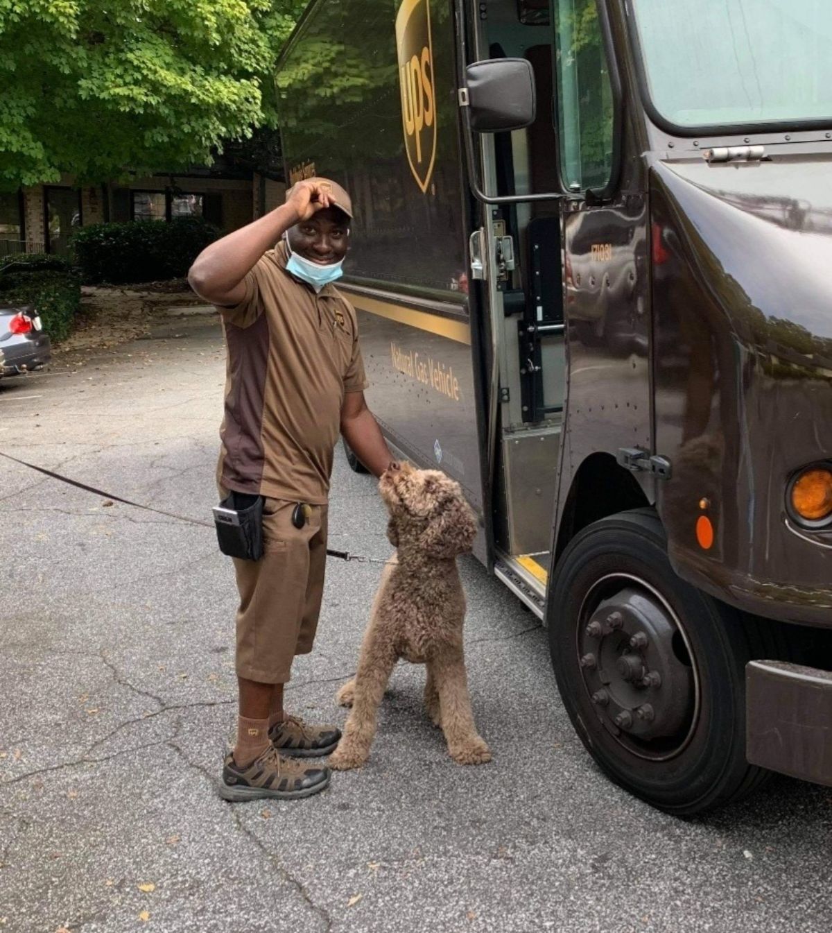 male ups driver standing next to the truck petting a brown fluffy dog