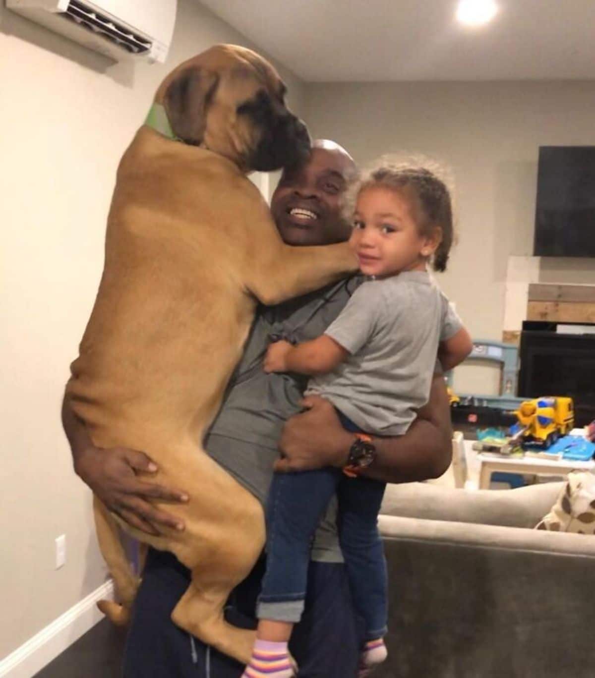 man carrying a large brown dog on his right and a little girl on his left