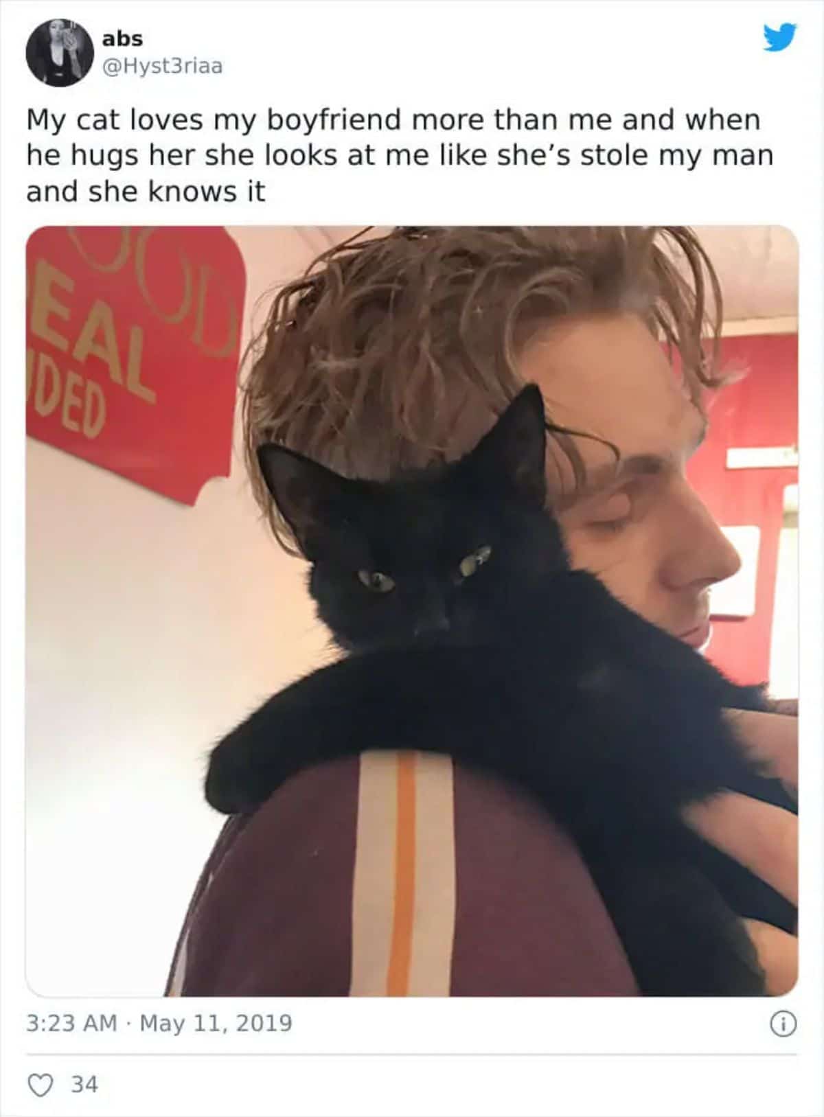 tweet with a photo showing a black cat gtting hugged by a man with the cat's head resting on his shoulder