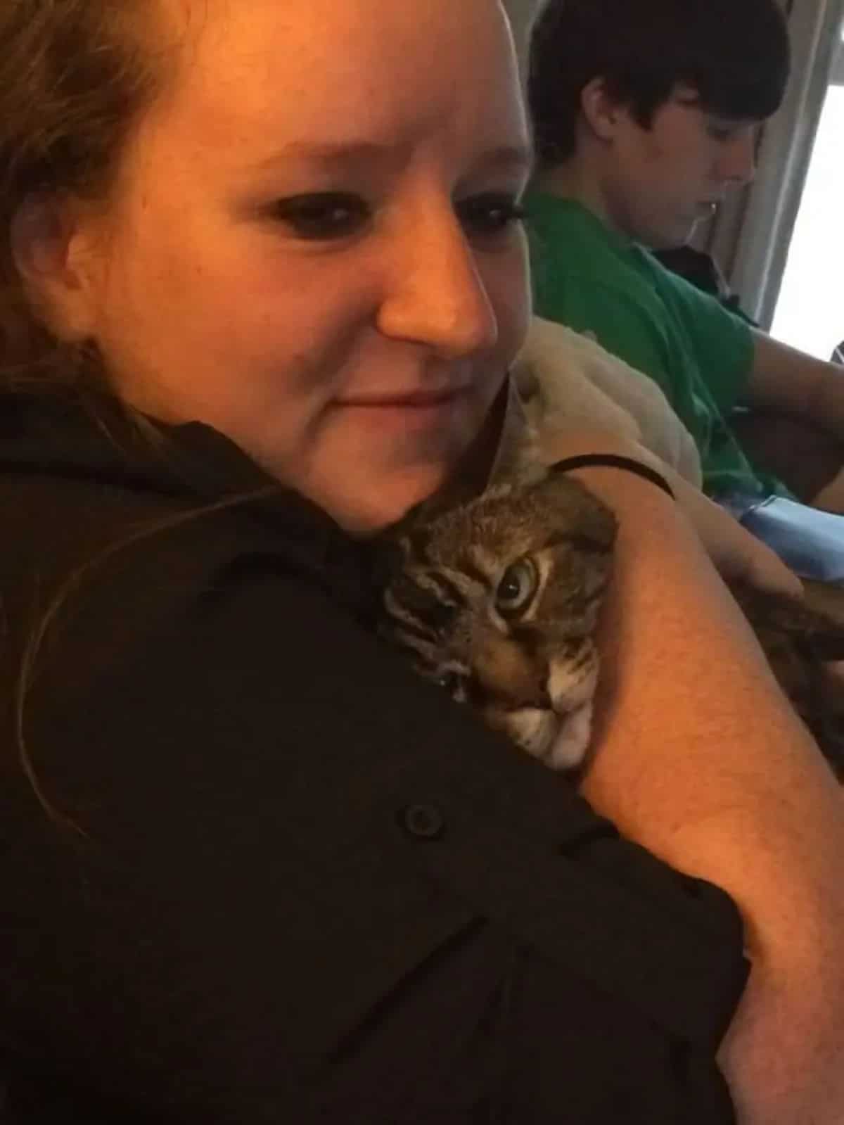 brown tabby getting hugged by a woman and looking annoyed