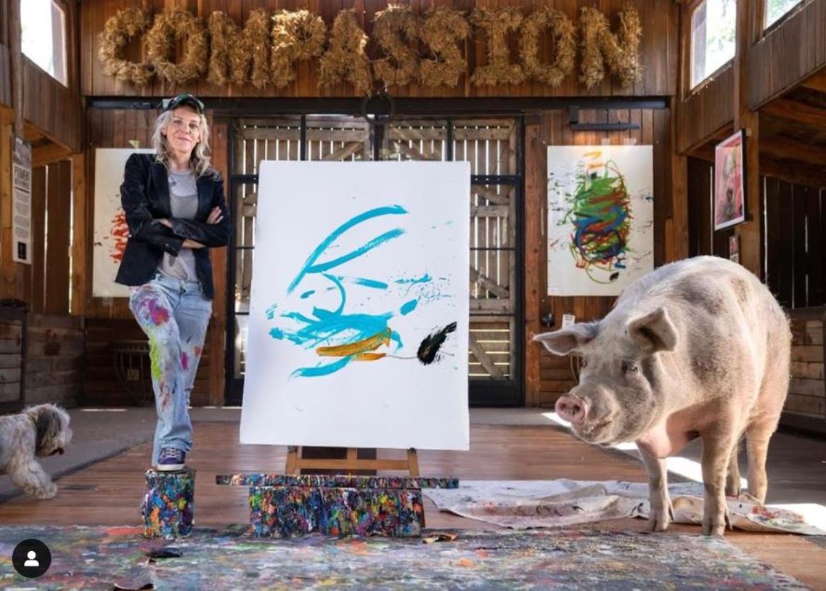 white pig and woman covered in paint standing on either side of a white canvas with blue yellow and black paint